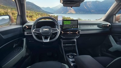 Внатрешноста на Dacia Duster со поглед на управувачот, централната конзола и дигиталниот дисплеј, со прекрасен пејсаж во позадина.