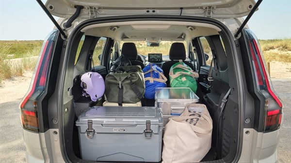 Отворениот багажен простор на Dacia Jogger со подигната петта врата, полн со опрема за патување и торби, со поглед на кабината и склопливите задни седишта.