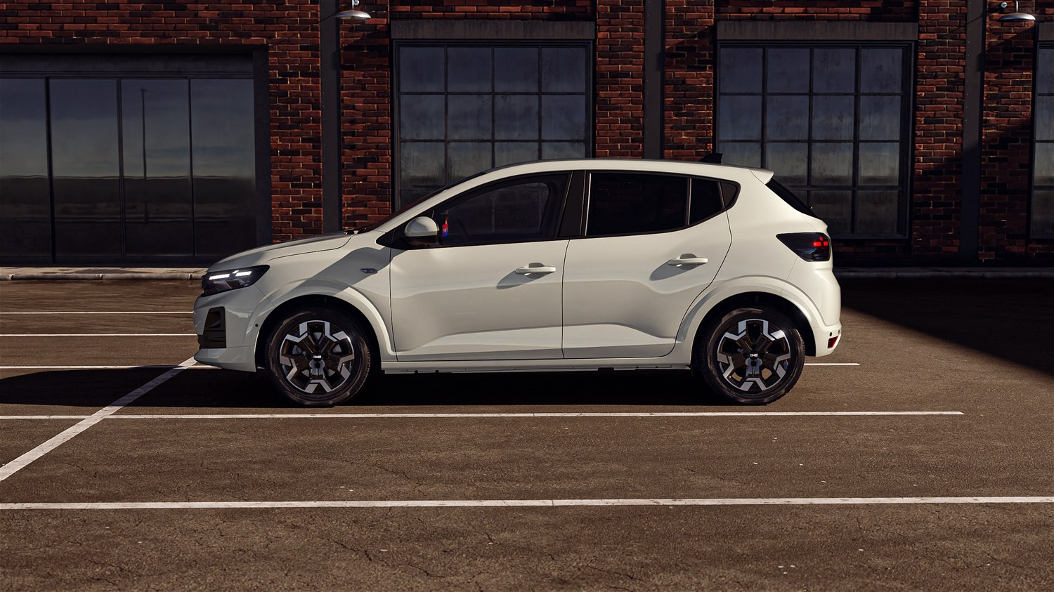 Dacia Sandero во профил во бела боја, паркирана на отворен паркинг пред зграда од црвена тула.