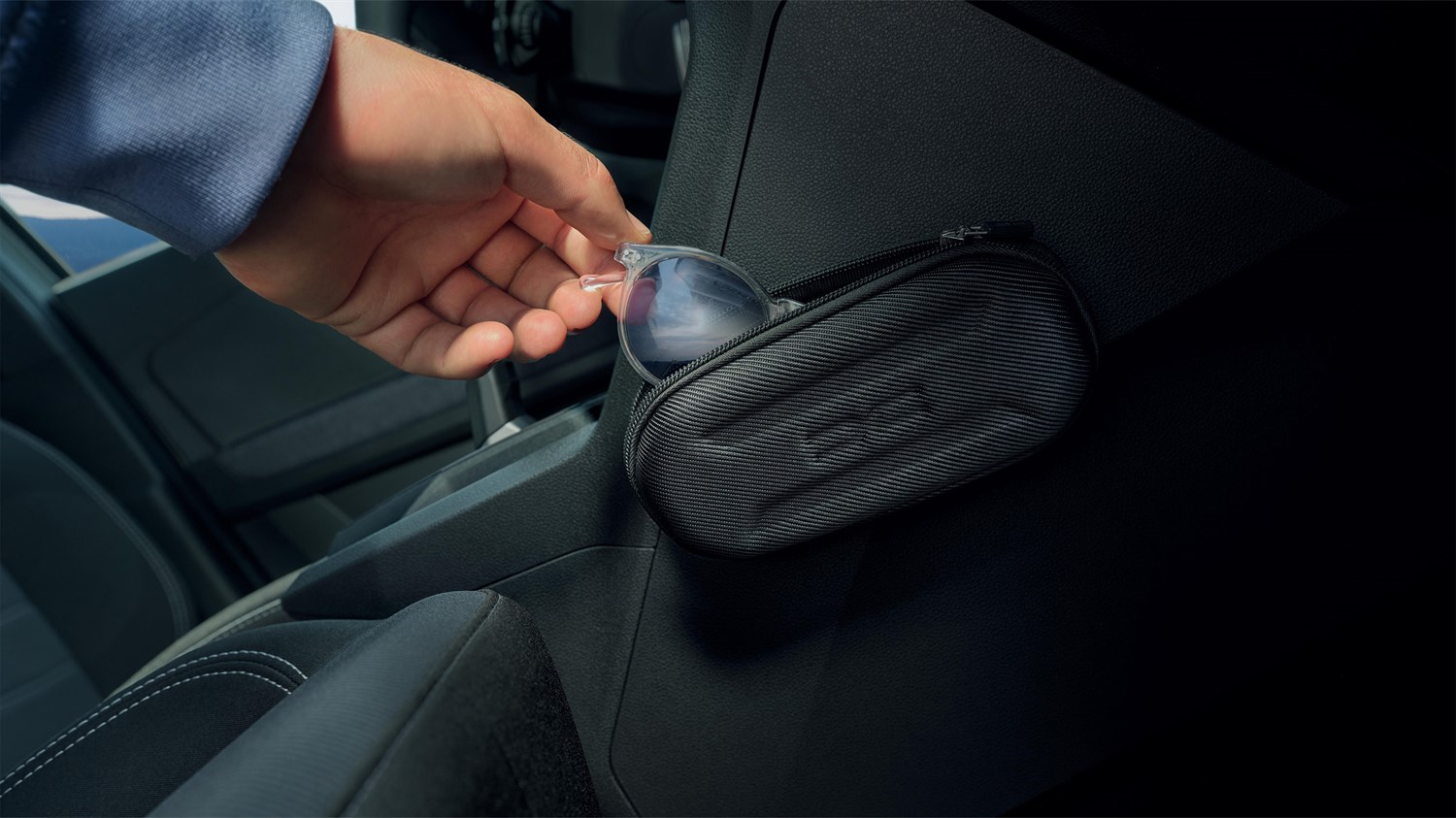 Рака што складира очила за сонце во футрола YouClip прикачена на внатрешноста на Dacia Sandero.