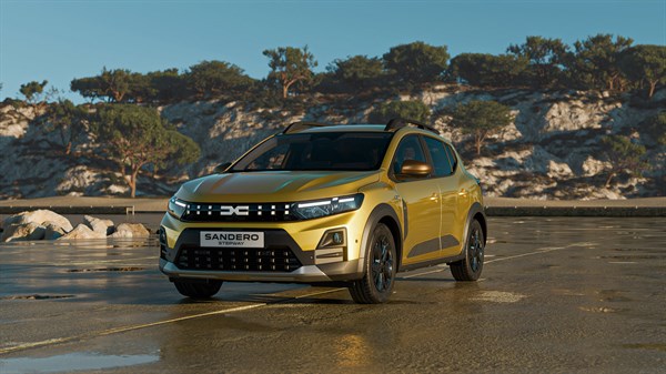 Dacia Sandero во жолта боја, прикажано од предната страна во сончево крајбрежно подрачје, со карпест пејзаж во позадина.