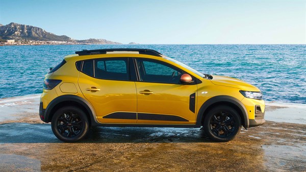 Dacia Sandero Stepway во жолта боја, фотографирано од страна покрај морето, паркирано на влажна бетонска површина.